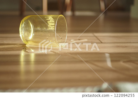 Spilled Water From Yellow Cup on Wooden Floor in Kitchen Spilled Water From Yellow Cup on Wooden Floor in Kitchen 122094255