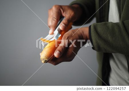 Manual peeling of a fresh carrot using a specialized vegetable peeler tool 122094257
