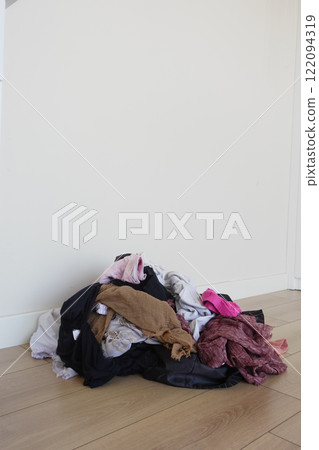 A Tumbling Pile of Unfolded Clothes Scattered on a Wooden Floor Surface A Tumbling Pile of Unfolded Clothes Scattered on a Wooden Floor Surface 122094319