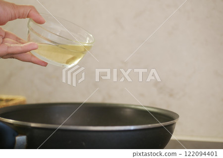Carefully pouring cooking oil into a pan as part of the preparation process Carefully pouring cooking oil into a pan as part of the preparation process 122094401