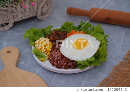 A vibrant meal consisting of red rice, meat, corn, carrots, lettuce, and a sunny side up egg A vibrant meal consisting of red rice, meat, corn, carrots, lettuce, and a sunny side up egg 122094542