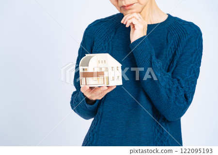 A worried senior woman holding a model house 122095193