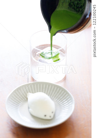 fresh matcha tea, green tea pouring on a glass of coconut water and Seal shape daifuku Japanese confectionery on wooden table. fresh matcha tea, green tea pouring on a glass of coconut water and Seal shape daifuku Japanese confectionery on wooden table. 122100245