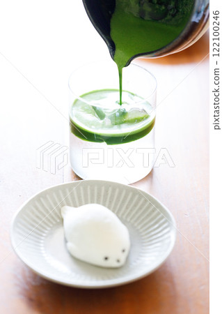 fresh matcha tea, green tea pouring on a glass of coconut water and Seal shape daifuku Japanese confectionery on wooden table. fresh matcha tea, green tea pouring on a glass of coconut water and Seal shape daifuku Japanese confectionery on wooden table. 122100246