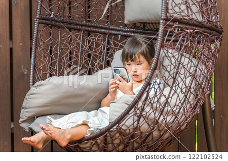 A girl sitting on a hanging chair and looking at her smartphone A girl sitting on a hanging chair and looking at her smartphone 122102524