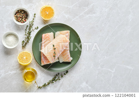 Overhead view of fresh cod fish fillets on a plate with herbs and citrus on a marble countertop 122104001