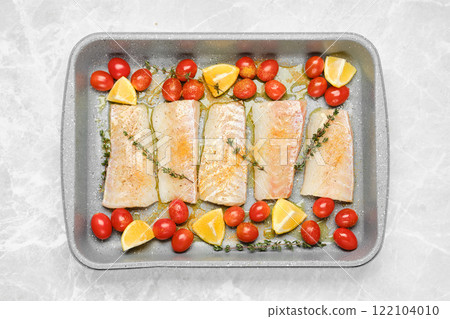 Top view of cod fish fillets on a baking tray with tomatoes and lemon wedges Top view of cod fish fillets on a baking tray with tomatoes and lemon wedges 122104010