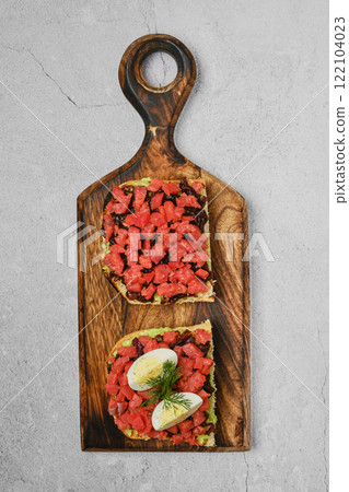 Delicious open-faced sandwiches topped with fresh ingredients on a wooden board 122104023