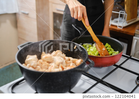 A person stirs vegetables in a red pan on the stove making the base for chicken stew 122104041