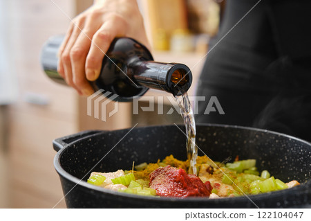 Cooking with fresh ingredients and adding wine to a pot for a delicious meal preparation 122104047