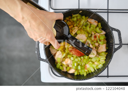 Cooking a savory dish with chicken and celery while adding seasoning in the kitchen 122104048