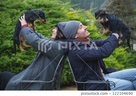 Couple lifting dachshund dogs while sitting back to back on chairs in garden Couple lifting dachshund dogs while sitting back to back on chairs in garden 122104690