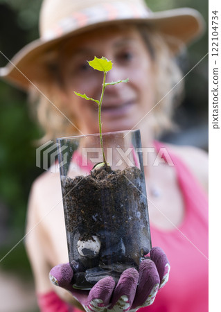 Gardener showing small holly oak sprout growing in glass jar Gardener showing small holly oak sprout growing in glass jar 122104734