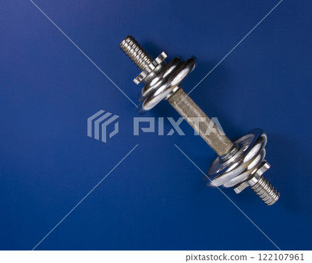 Stainless metal dumbbell on dark blue background with copyspace for text 122107961