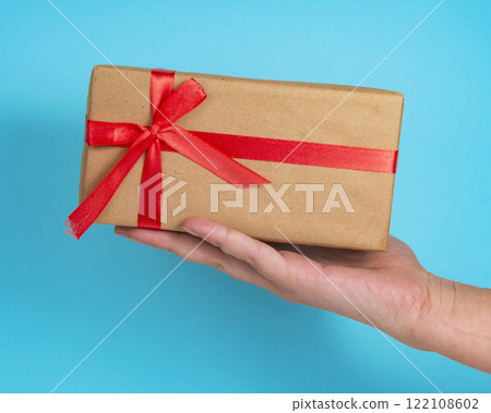 Gift box craft paper with red bow in hand on blue background 122108602