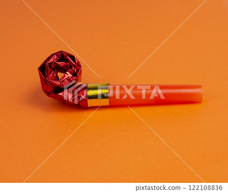 Party foil red horn noisemaker for carnival on the orange background Party foil red horn noisemaker for carnival on the orange background 122108836