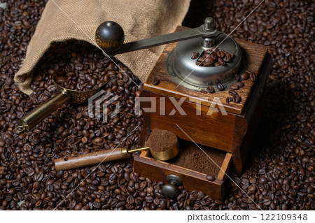 Rustic coffee grinder with a measuring spoon and a bag of coffee with a coffee scoop on a background  of coffee beans 122109348