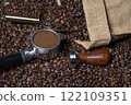 Jute sack full of coffee with a golden coffee scoop and a tamper and a coffee portafilter on a background of many coffee beans 122109351