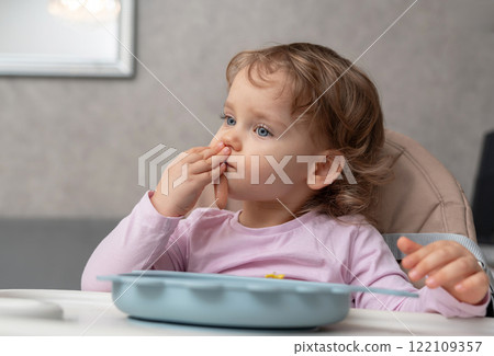 A toddler enjoying her meal with a focused expression in a cozy home setting A toddler enjoying her meal with a focused expression in a cozy home setting 122109357