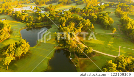 A panoramic aerial view of a golf course with ponds and lush greenery illuminated by golden sunlight 122109369