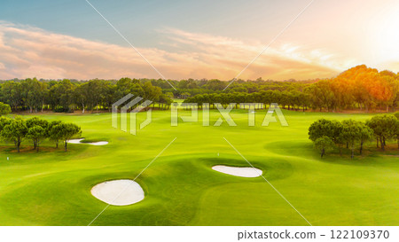 A golf course illuminated by golden sunset light with sand traps and vibrant greenery A golf course illuminated by golden sunset light with sand traps and vibrant greenery 122109370