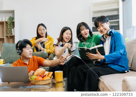 Asian college student reading a book study on laptop prepare for the exam or work on a group project at home. 122109733