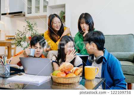 Asian college student reading a book study on laptop prepare for the exam or work on a group project at home. 122109738