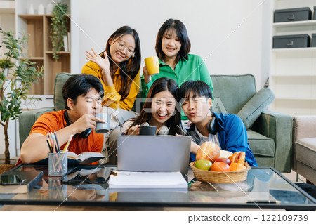 Asian college student reading a book study on laptop prepare for the exam or work on a group project at home. 122109739