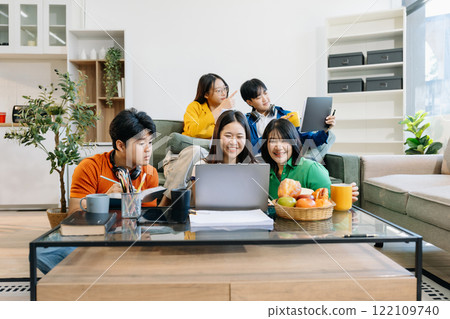 Asian college student reading a book study on laptop prepare for the exam or work on a group project at home. Asian college student reading a book study on laptop prepare for the exam or work on a group project at home. 122109740