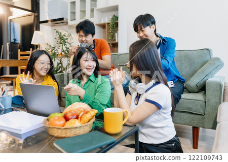 Asian college student reading a book study on laptop prepare for the exam or work on a group project at home. 122109743
