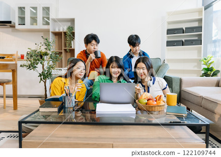 Asian college student reading a book study on laptop prepare for the exam or work on a group project at home. Asian college student reading a book study on laptop prepare for the exam or work on a group project at home. 122109744