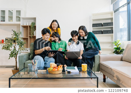 Asian college student reading a book study on laptop prepare for the exam or work on a group project at home. 122109748
