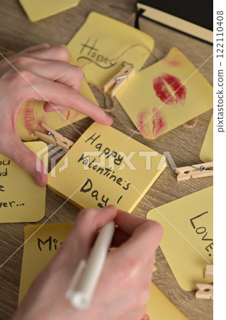 Woman's hand writing romantic message for Valentine's Day on many yellow sticker papers with lipstick kiss mark and cute inscriptions. Preparation to celebration Woman's hand writing romantic message for Valentine's Day on many yellow sticker papers with lipstick kiss mark and cute inscriptions. Preparation to celebration 122110408