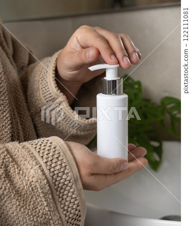 Close up of hands in brown bathrobe pumping soap from a cosmetic bottle, mockup 122111081