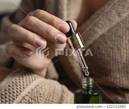 Closeup of woman in brown bathrobe opening green dropper bottle, cosmetic mockup Closeup of woman in brown bathrobe opening green dropper bottle, cosmetic mockup 122111085