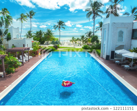 Aerial view of young woman on swimming ring in pool, green palms 122111151