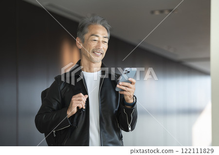 A man in his 60s carrying a backpack looking at his smartphone screen A man in his 60s carrying a backpack looking at his smartphone screen 122111829