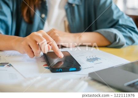 Close-up of a person using a smartphone to review financial documents and charts, highlighting modern business analysis. Close-up of a person using a smartphone to review financial documents and charts, highlighting modern business analysis. 122111976