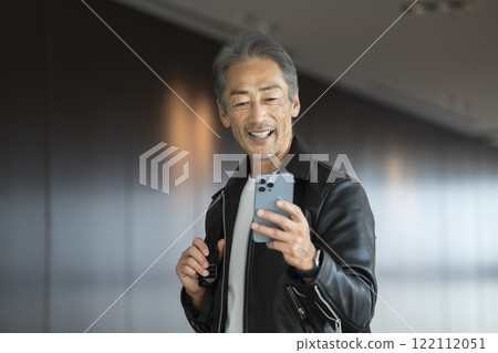 A smiling man in his 60s looking at his smartphone screen 122112051