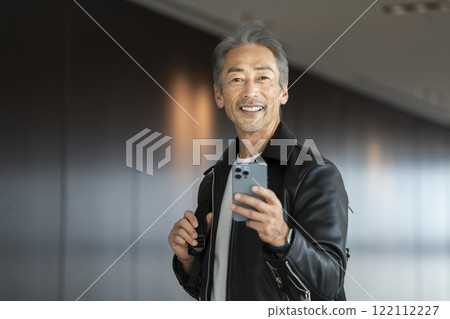 60 多歲的微笑男子拿著智慧型手機，看著相機，肖像 122112227