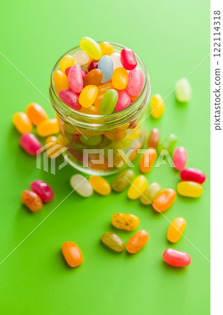 Multicolored jelly beans with various flavors in jar on green background. 122114318