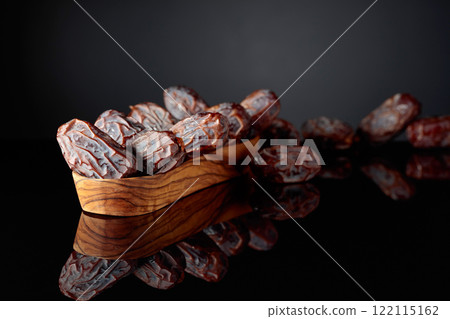 Dates fruits in a wooden dish on a black background. Dates fruits in a wooden dish on a black background. 122115162