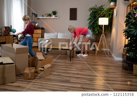 Two Women Unpacking a Variety of Boxes Together in a Cozy and Inviting Living Room Space 122115358