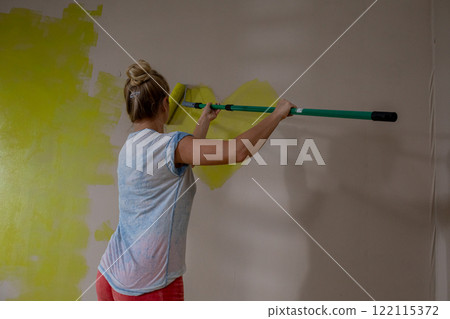 A Person is Painting a Wall Using a Roller That is Coated in a Bright Yellow Color 122115372
