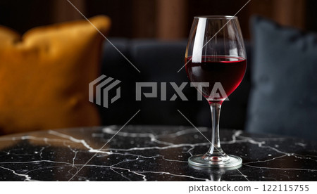 Elegant glass of red wine on a marble table with plush pillows in a cozy interior setting Elegant glass of red wine on a marble table with plush pillows in a cozy interior setting 122115755