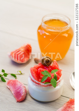 homemade sweet yogurt in a glass jar with pieces of red ripe grapefruit and honey, on a wooden table 122117166