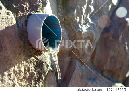 Icicle Forming at a Drain Pipe During Winter Near a Rocky Wall Icicle Forming at a Drain Pipe During Winter Near a Rocky Wall 122117315