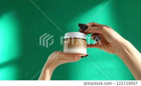 Beautician holding cosmetic cream jar on green background 122118087