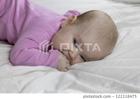 Cute and beautiful 4-month-old baby girl laying on bed. Infant in pink bodysuit on bed against white background. 122118475