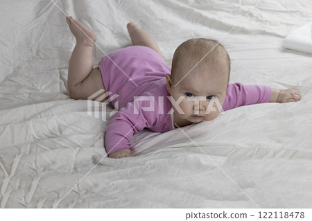 Cute and beautiful 4-month-old baby girl laying on bed. Infant in pink bodysuit on bed against white background. 122118478